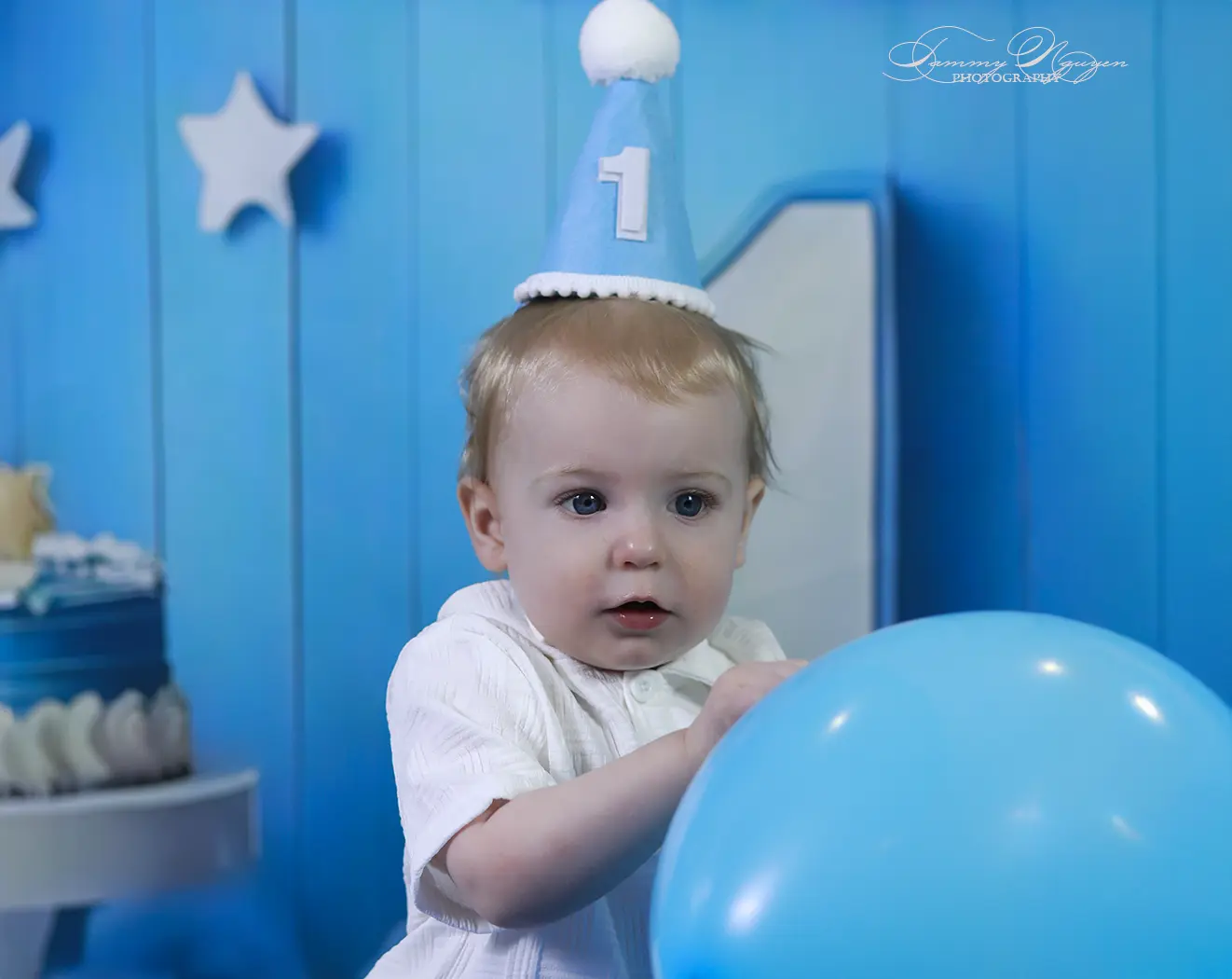 A one-year-old child playing with a blue balloon during a birthday portrait session.