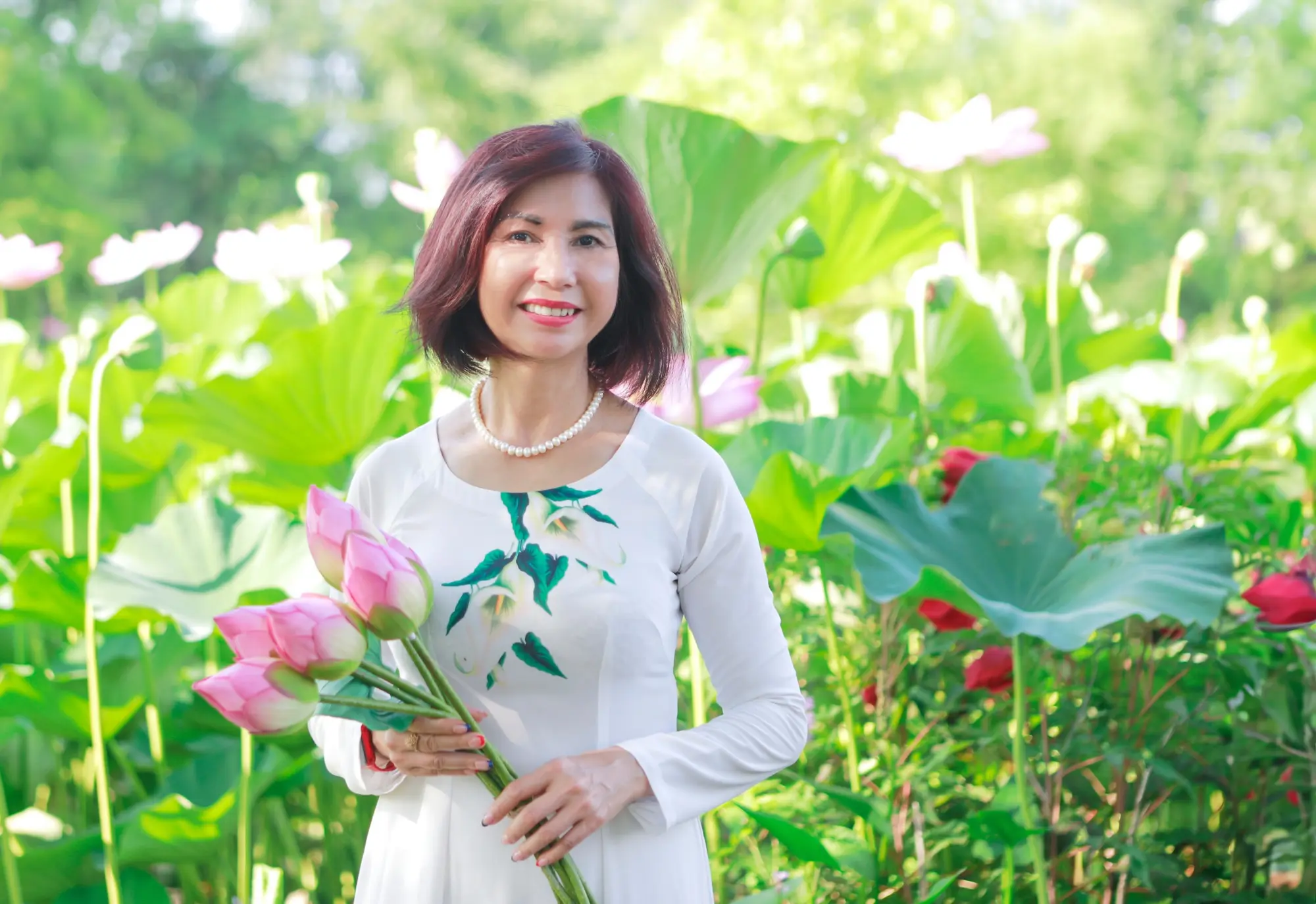 A woman holding pink lotus flowers in a sunlit lotus garden.