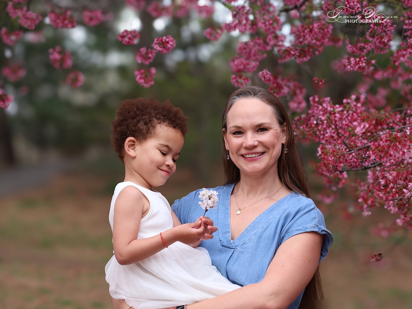 Mother holding her young daughter under a blossoming tree.