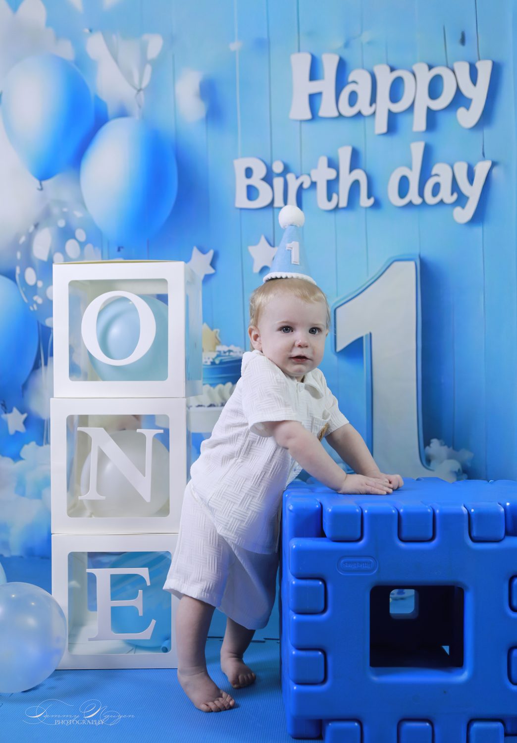 A one-year-old in a party hat beside lettered blocks.