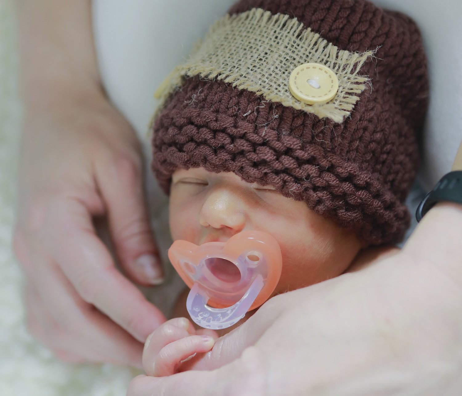 A sleeping newborn in a hand-knit cap holding a parent's finger, photographed in Falls Church, Virginia.