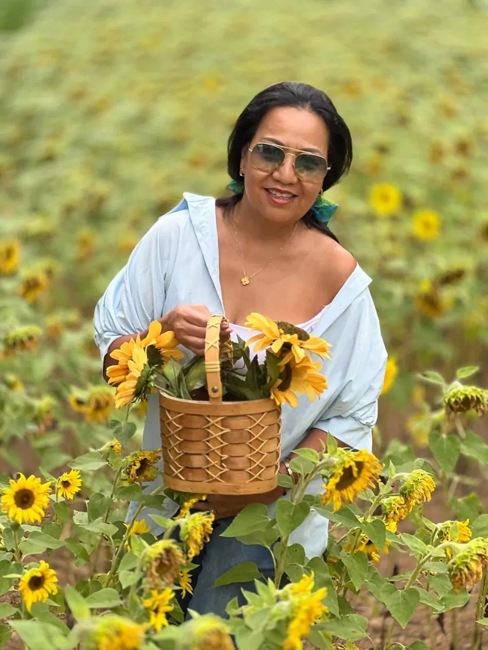 A woman in a sunflower field holding a basket of sunflowers.