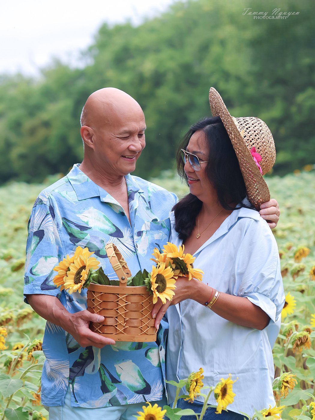 A couple smiling at each other in a sunflower field in Northern Virginia, holding a basket of sunflowers.