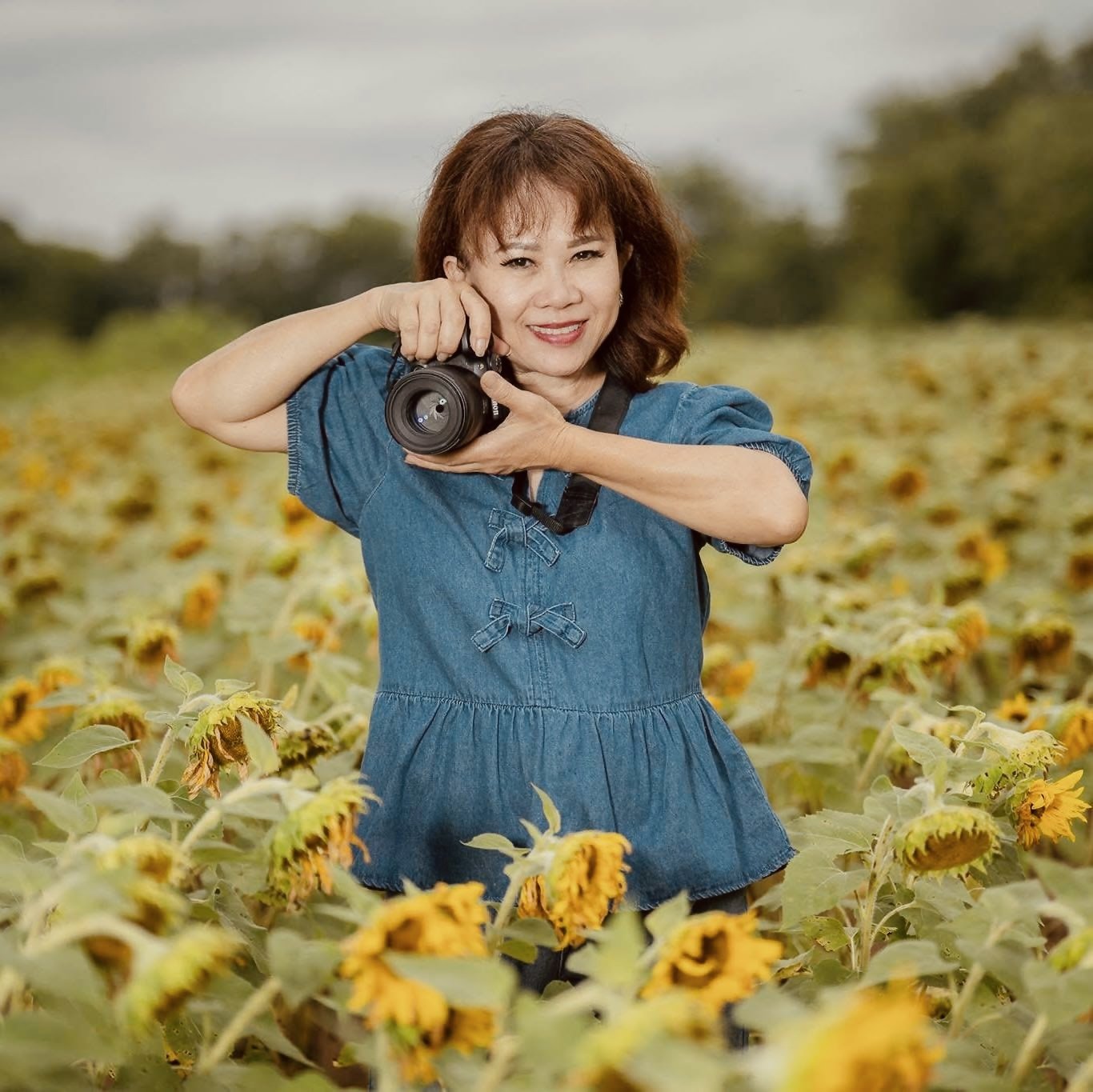Tammy Nguyen holding her camera, photographing in a sunflower field.